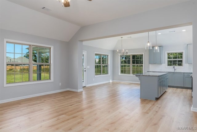 kitchen featuring open floor plan, a sink, vaulted ceiling, gray cabinets, and backsplash