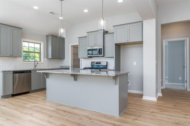 kitchen featuring appliances with stainless steel finishes, a kitchen breakfast bar, light stone countertops, gray cabinetry, and light wood-style floors