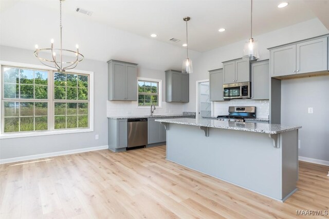 kitchen with light stone counters, baseboards, gray cabinetry, appliances with stainless steel finishes, and a kitchen breakfast bar