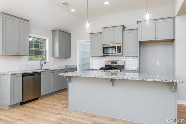 kitchen featuring a breakfast bar area, stainless steel appliances, visible vents, gray cabinetry, and a sink