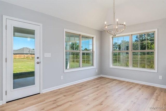 unfurnished dining area with plenty of natural light, light wood-style flooring, baseboards, and an inviting chandelier