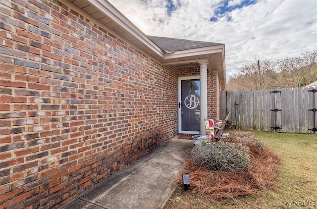 view of exterior entry with brick siding and fence