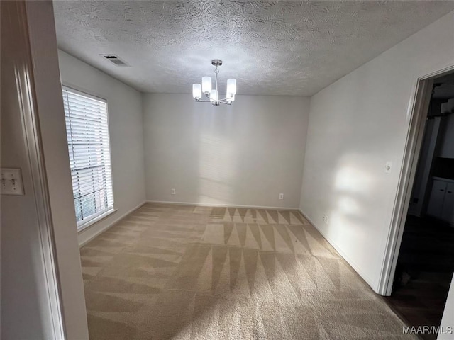 carpeted empty room featuring a notable chandelier, a healthy amount of sunlight, and a textured ceiling