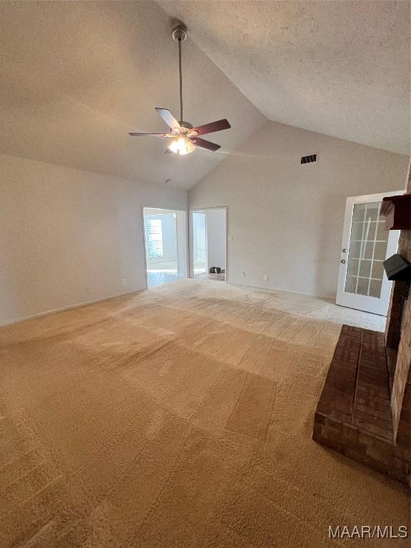 unfurnished living room with carpet, a textured ceiling, a brick fireplace, and lofted ceiling