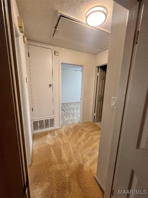 hallway featuring light colored carpet and a textured ceiling