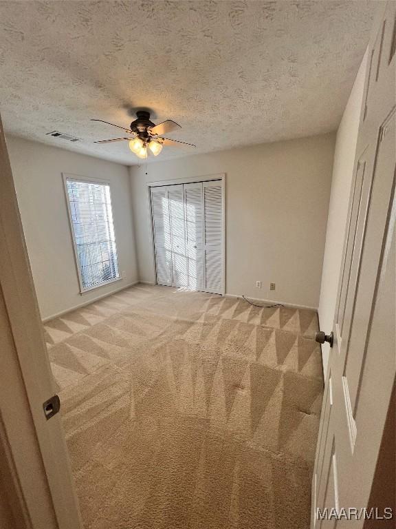 unfurnished bedroom with a textured ceiling, light colored carpet, and ceiling fan