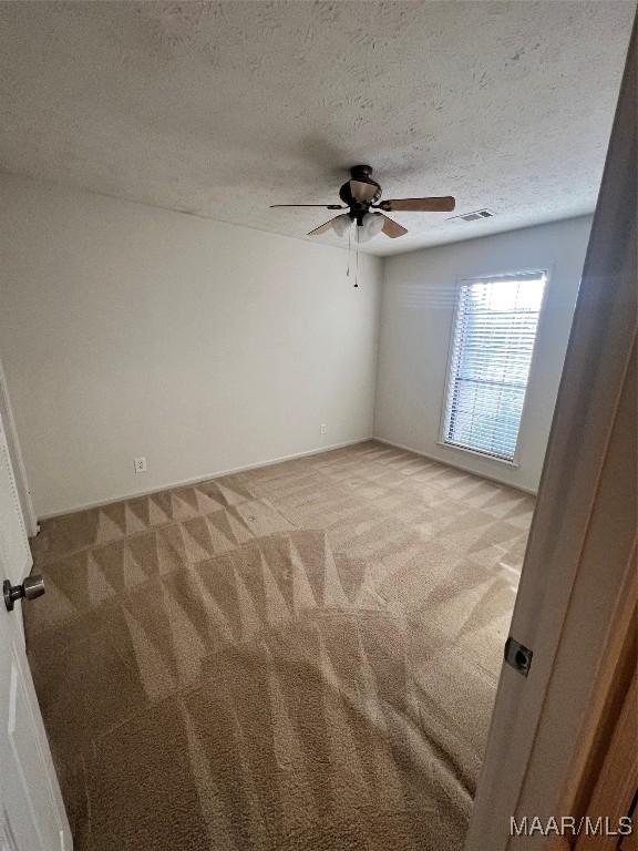 unfurnished room featuring ceiling fan, light colored carpet, and a textured ceiling