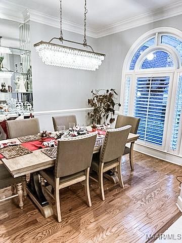 dining area with hardwood / wood-style flooring, ornamental molding, and an inviting chandelier