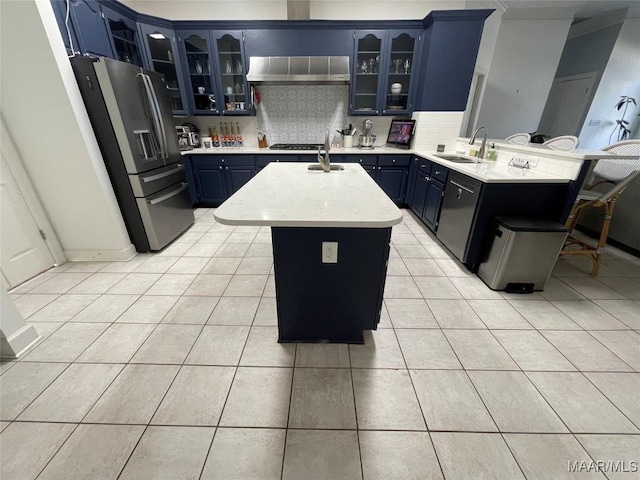 kitchen featuring a center island with sink, wall chimney range hood, sink, blue cabinetry, and stainless steel appliances