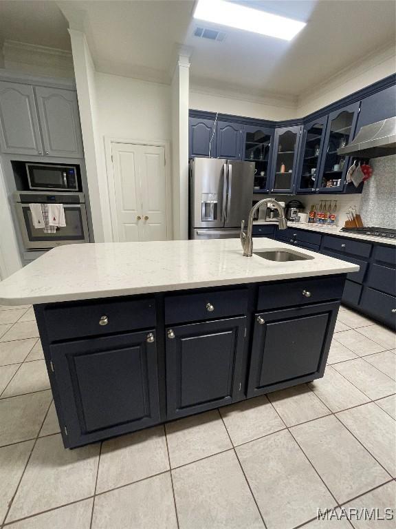 kitchen with appliances with stainless steel finishes, light tile patterned floors, a kitchen island with sink, and sink