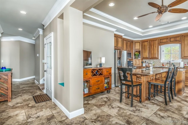 kitchen featuring stainless steel fridge, tasteful backsplash, ornamental molding, and a breakfast bar area