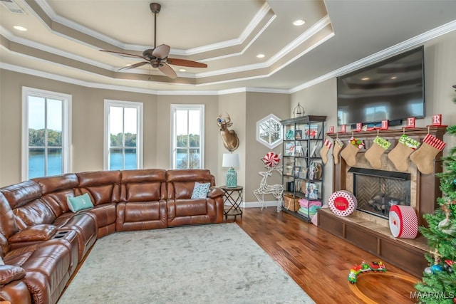 living room featuring a raised ceiling, a tile fireplace, crown molding, and wood-type flooring