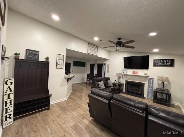 living room featuring ceiling fan, a textured ceiling, and light wood-type flooring