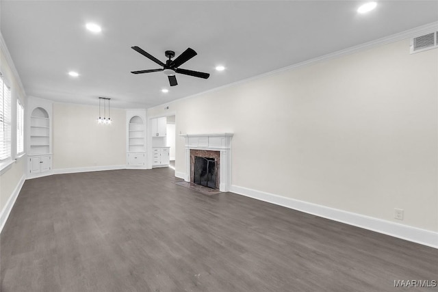 unfurnished living room with built in shelves, crown molding, a fireplace, and dark hardwood / wood-style floors