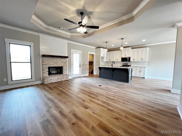 unfurnished living room featuring a raised ceiling, ornamental molding, a healthy amount of sunlight, and light wood-type flooring