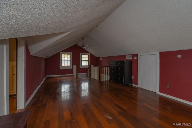 additional living space with a textured ceiling, dark wood-type flooring, and lofted ceiling