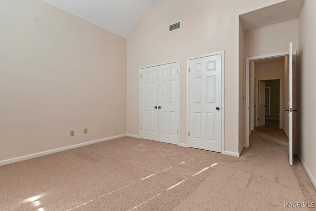 unfurnished bedroom with multiple closets, light carpet, and lofted ceiling