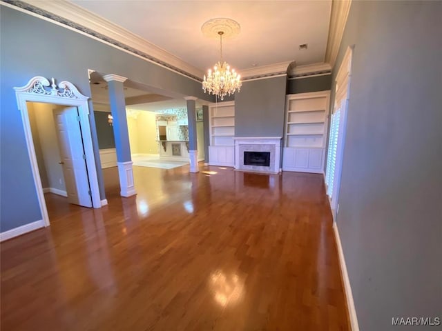 unfurnished living room featuring decorative columns, ornamental molding, wood-type flooring, built in features, and an inviting chandelier