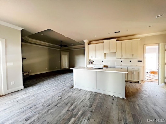 kitchen with white cabinetry, ceiling fan, hardwood / wood-style flooring, a center island with sink, and crown molding