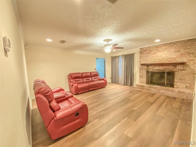 living room featuring ceiling fan, wood-type flooring, a textured ceiling, and a brick fireplace