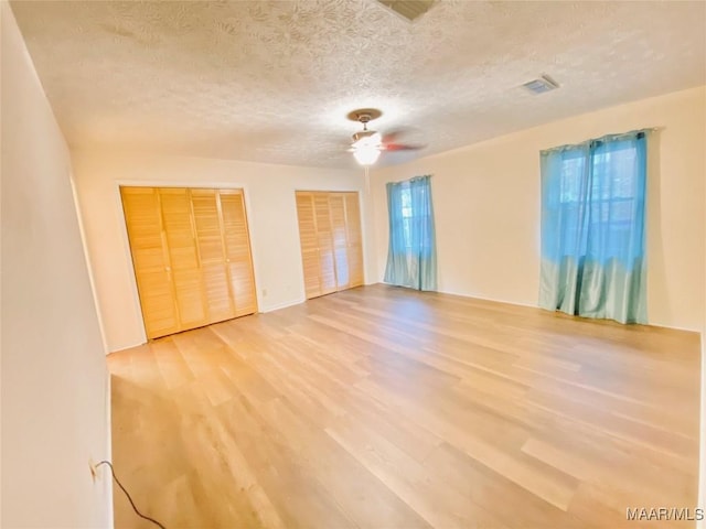 unfurnished bedroom featuring a textured ceiling, hardwood / wood-style flooring, ceiling fan, and multiple closets