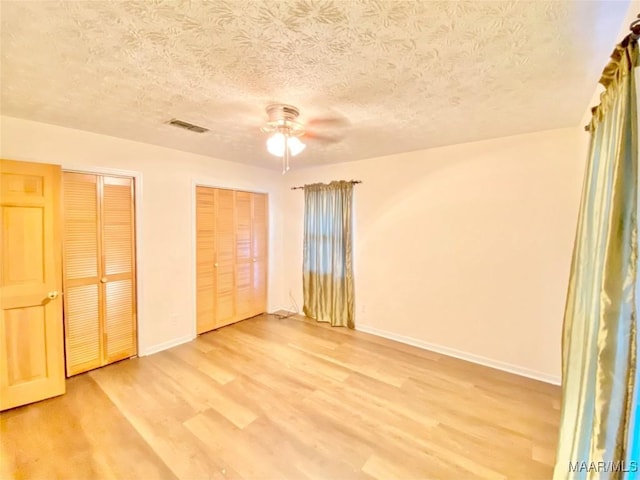 unfurnished bedroom featuring ceiling fan, wood-type flooring, a textured ceiling, and multiple closets