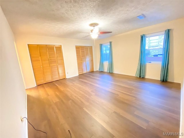 unfurnished bedroom featuring hardwood / wood-style floors, ceiling fan, a textured ceiling, and multiple closets