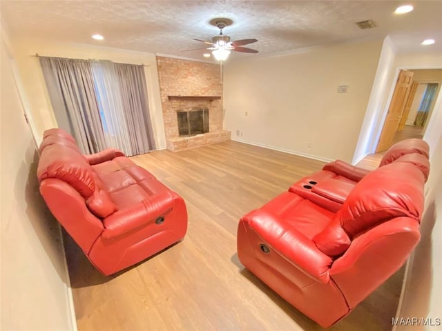 living room with ceiling fan, wood-type flooring, a textured ceiling, and a brick fireplace