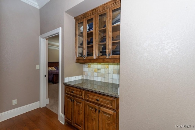 kitchen featuring backsplash, dark hardwood / wood-style floors, ornamental molding, and dark stone countertops