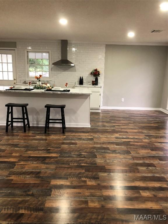 kitchen with a breakfast bar, dark wood-type flooring, wall chimney exhaust hood, tasteful backsplash, and white cabinetry