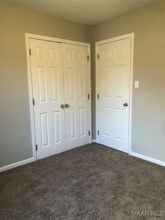 unfurnished bedroom with dark carpet and a closet