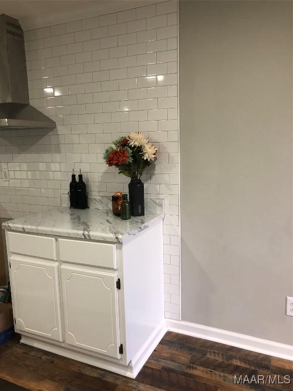 bar with decorative backsplash, white cabinetry, dark wood-type flooring, and wall chimney range hood