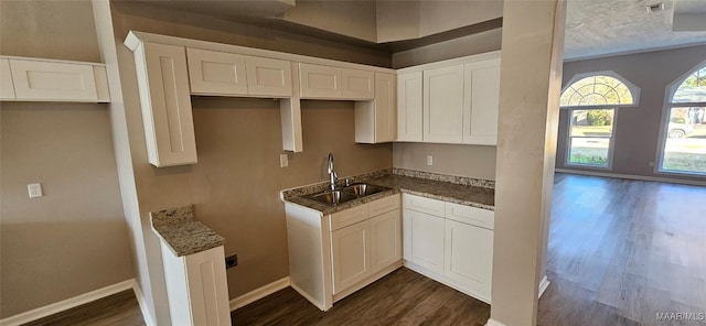 kitchen with dark stone counters, white cabinetry, sink, and dark wood-type flooring