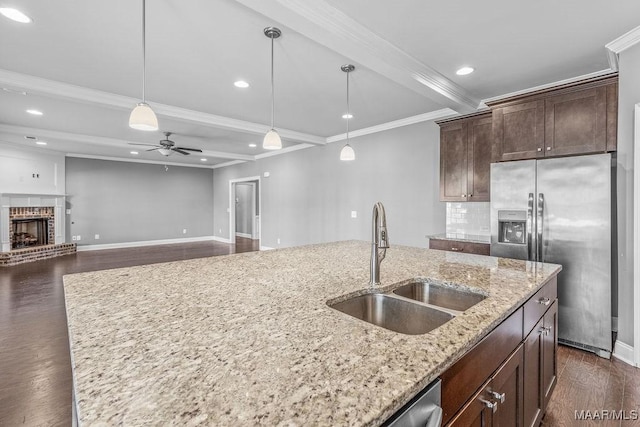 kitchen with light stone countertops, ceiling fan, sink, stainless steel fridge with ice dispenser, and an island with sink