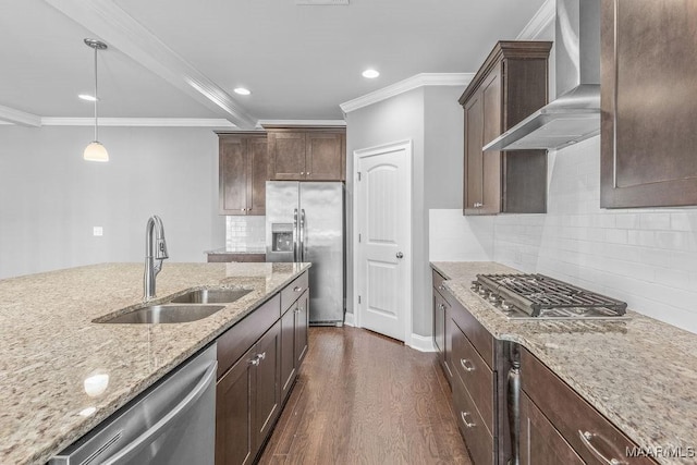 kitchen with light stone countertops, appliances with stainless steel finishes, wall chimney exhaust hood, sink, and hanging light fixtures