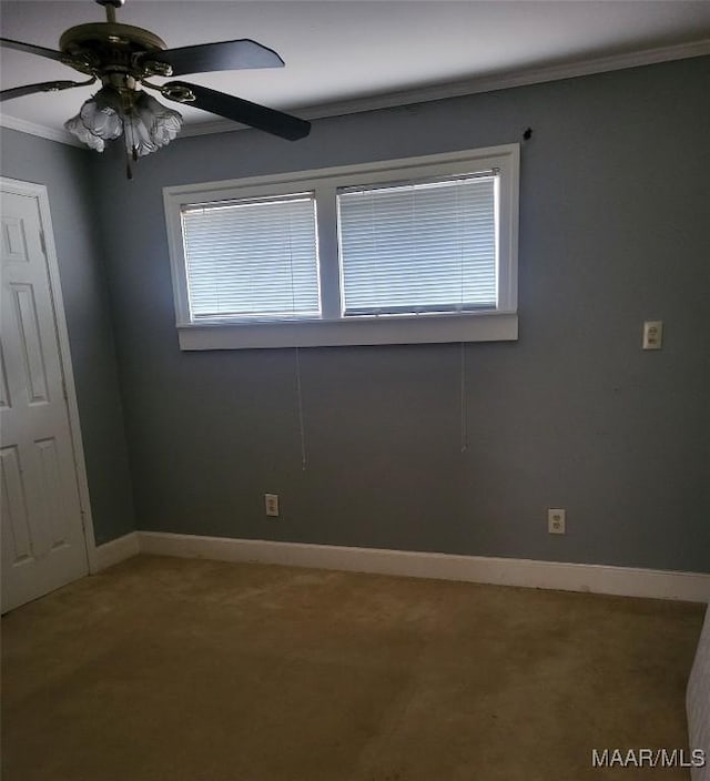 empty room featuring a ceiling fan, carpet flooring, crown molding, and baseboards