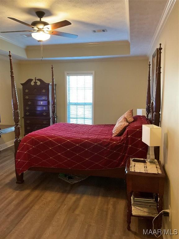 bedroom with hardwood / wood-style floors, a raised ceiling, ceiling fan, and ornamental molding