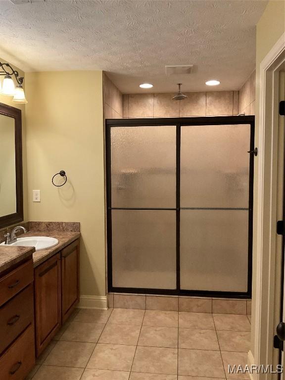 bathroom featuring tile patterned floors, vanity, a shower with shower door, and a textured ceiling