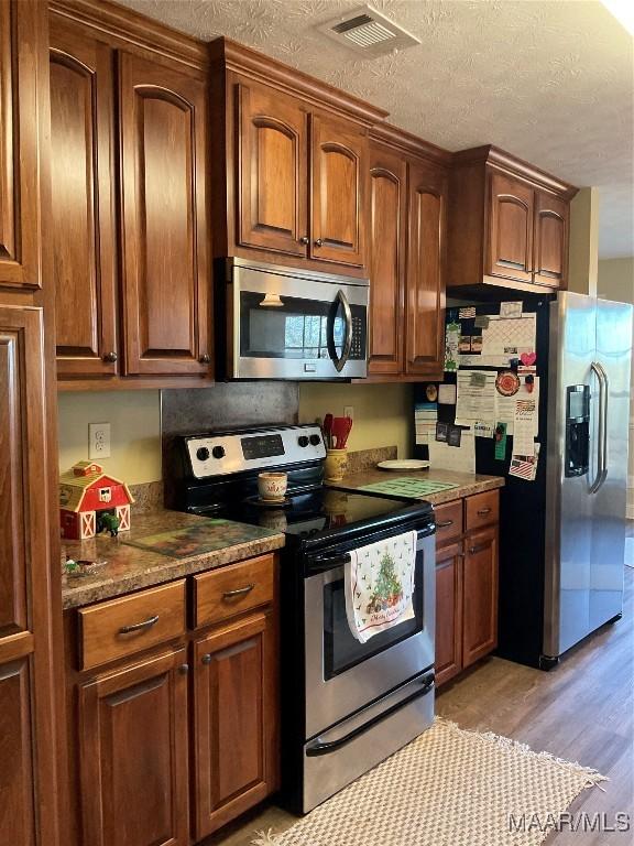 kitchen featuring dark stone countertops, light wood-type flooring, a textured ceiling, and appliances with stainless steel finishes