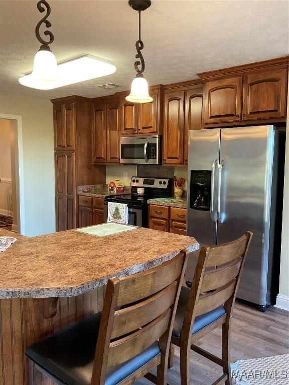 kitchen featuring a breakfast bar, appliances with stainless steel finishes, pendant lighting, and wood-type flooring