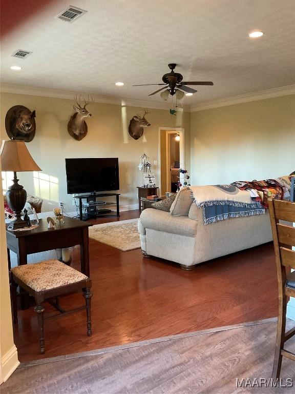 living room featuring crown molding, ceiling fan, wood-type flooring, and a textured ceiling