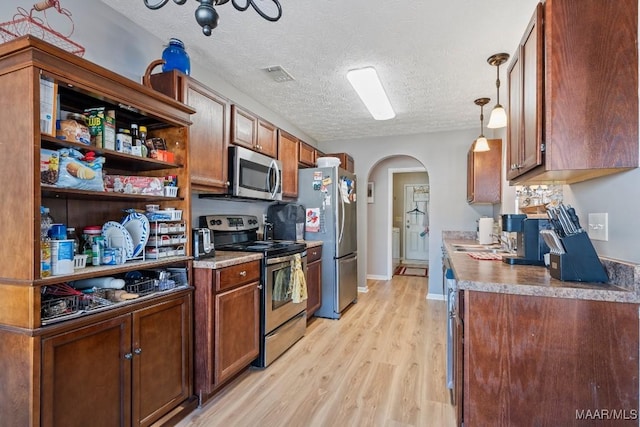 kitchen with sink, pendant lighting, a textured ceiling, appliances with stainless steel finishes, and light wood-type flooring