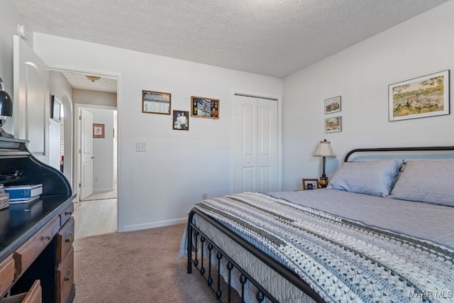 bedroom with a textured ceiling, light colored carpet, and a closet