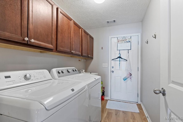 laundry room featuring cabinets, a textured ceiling, sink, light hardwood / wood-style flooring, and washing machine and clothes dryer