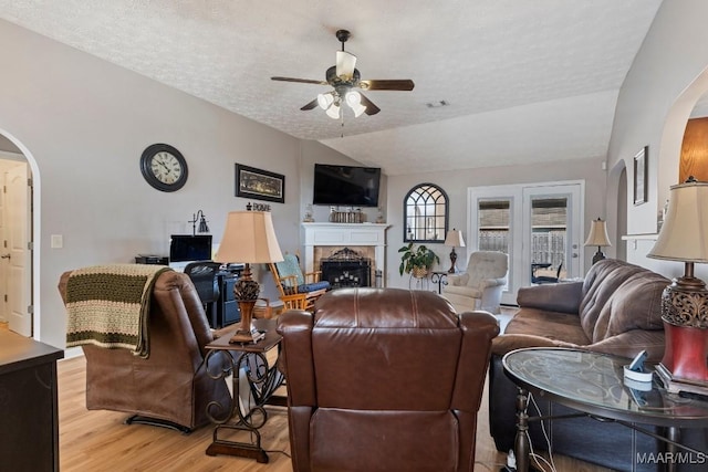 living room with a textured ceiling, vaulted ceiling, ceiling fan, light hardwood / wood-style flooring, and a fireplace