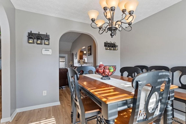 dining space featuring light hardwood / wood-style flooring, a textured ceiling, and a notable chandelier