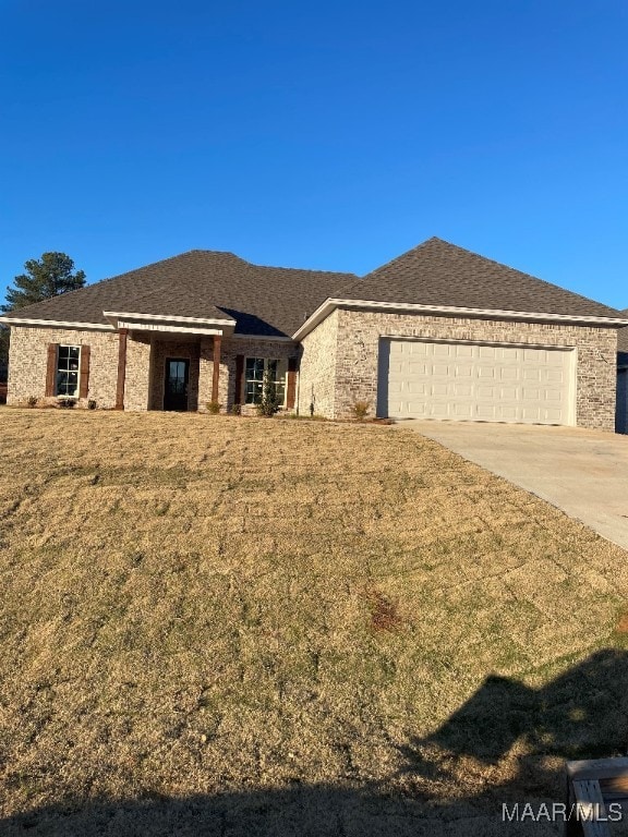 view of front of property featuring a garage, a shingled roof, a front lawn, and concrete driveway