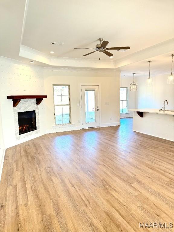 unfurnished living room with a fireplace, a tray ceiling, and wood finished floors