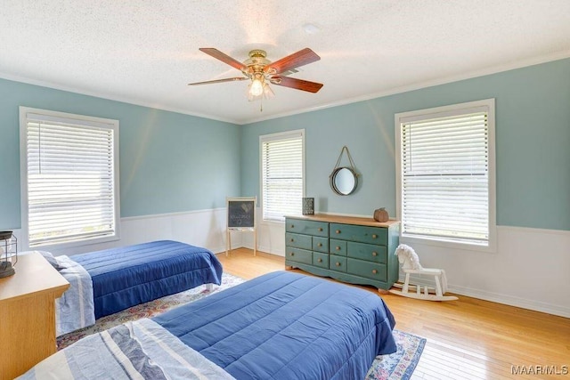 bedroom featuring ceiling fan, light hardwood / wood-style floors, a textured ceiling, and ornamental molding