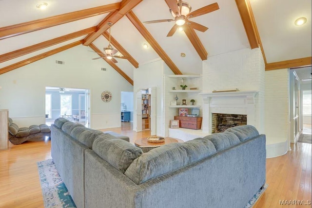 living room featuring beam ceiling, a large fireplace, high vaulted ceiling, and light hardwood / wood-style flooring